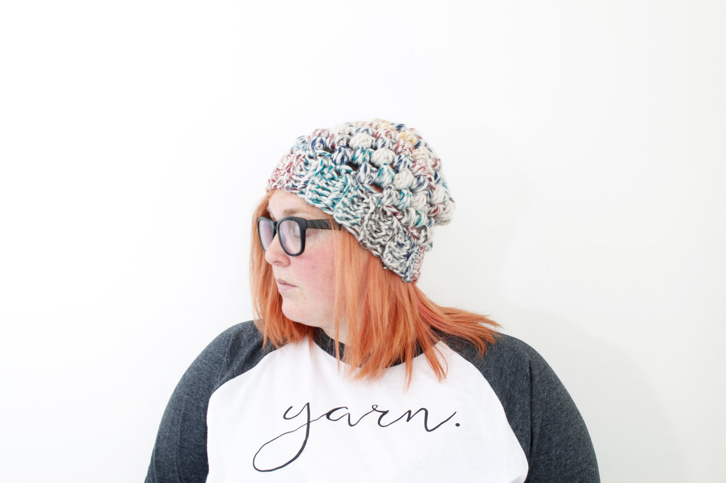 chunky rainbow color puff stitch beanie on model with peach hair and black glasses