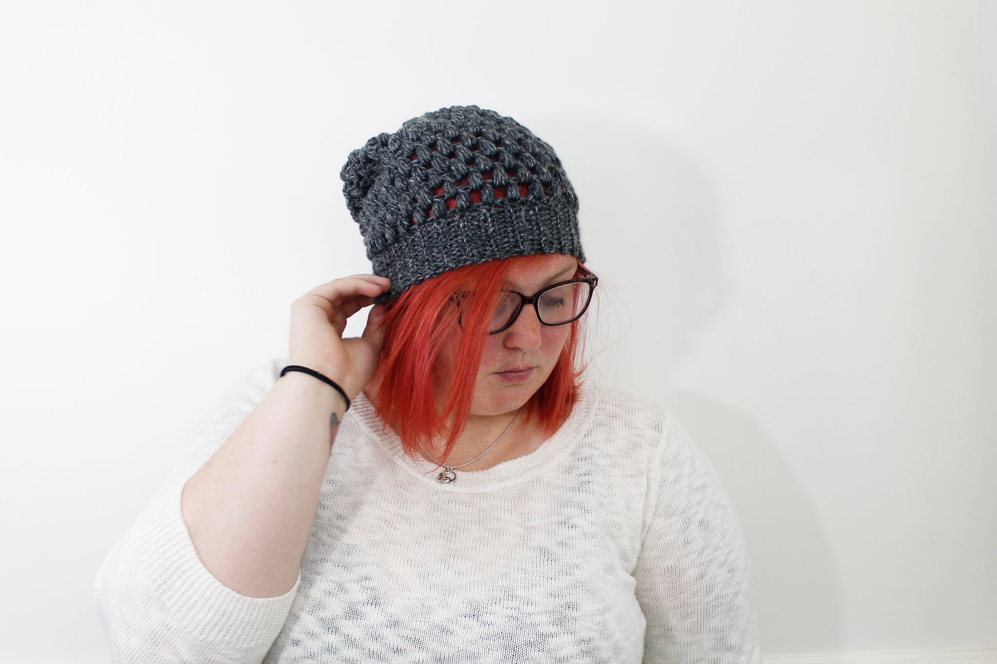 Dark gray puff stitch beanie showing the slouch of the hat on a model with thick black glasses and bright neon red hair.