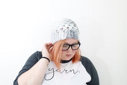 chunky puff stitch beanie in variegated shades of white and gray on model with black glasses and peach hair